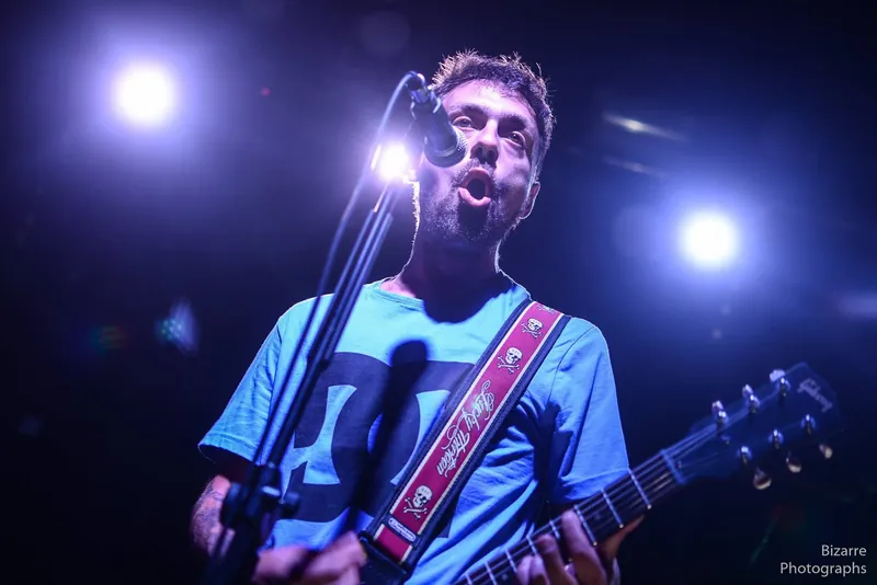 Cantante con guitarra cantando al micrófono bajo luces azules en Entriopia Fest