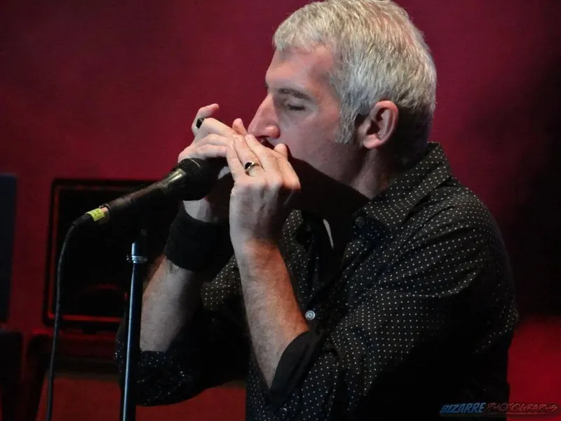 Cantante de Buitres tocando la armónica al micrófono con luz roja