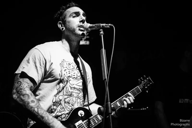 Guitarrista tatuado cantando en Entriopia, en blanco y negro