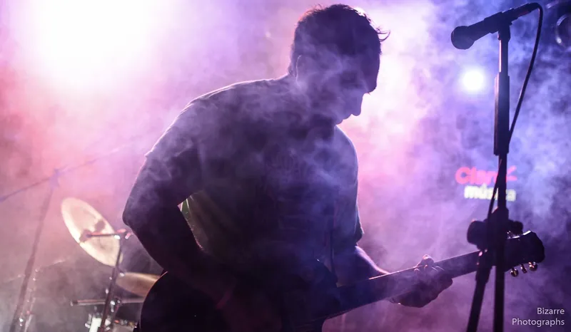Guitarrista entre humo violeta frente al micrófono en Entriopia Fest